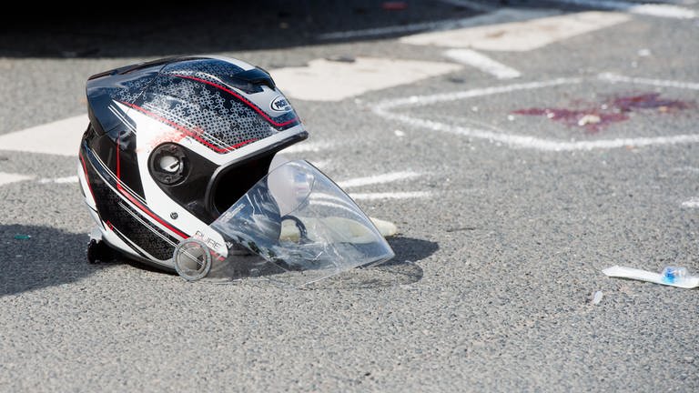 Ein beschädigter Helm liegt nach einem schweren Motorradunfall auf einer Straße  (Foto: dpa Bildfunk, picture alliance / dpa | Julian Stratenschulte)
